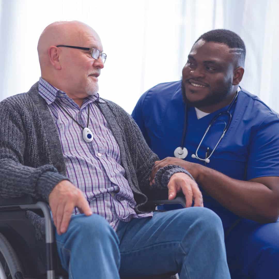 Man in wheelchair wearing lifeline button talking to healthcare worker